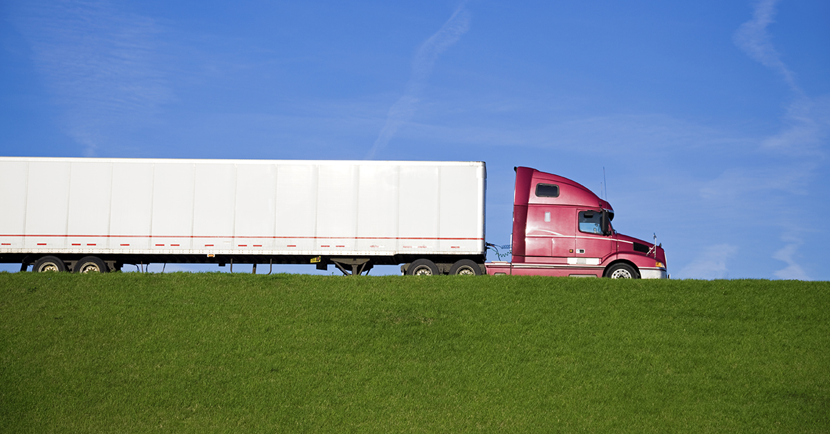 Red tractor trailer acting as part of supply chain against grass and blue sky.