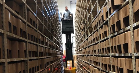 A fork truck maneuvers through a tight corridor in a warehouse.